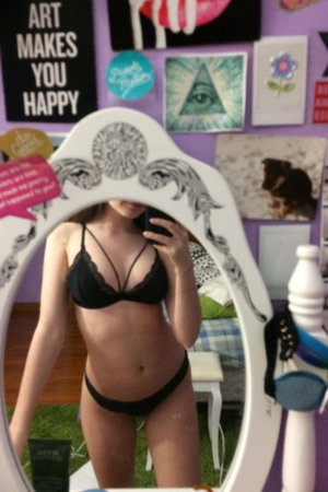 Woman in black lingerie taking mirror selfie in bedroom.