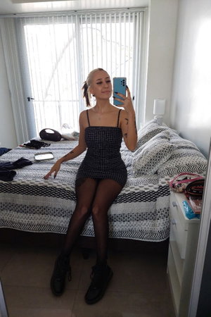 Woman in black dress taking selfie on bed in bedroom.