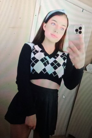 Woman in black and white argyle crop top and black skirt taking mirror selfie indoors.
