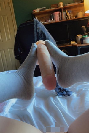 Person in socks holding a dildo on a bed in a bedroom.