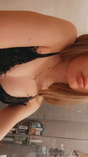 Woman with blonde hair in black lace lingerie, posing in bathroom mirror selfie.