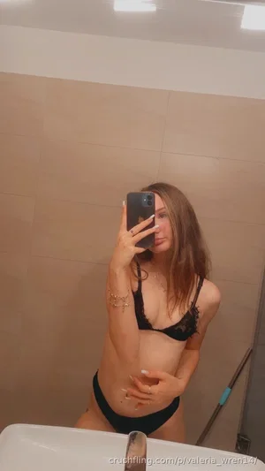 Woman in black lace lingerie taking mirror selfie in bathroom.