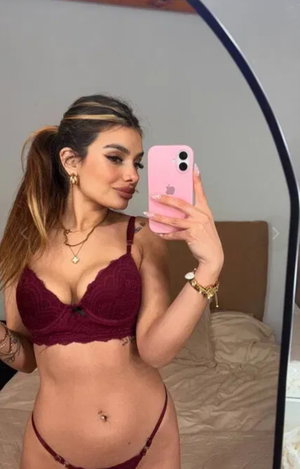 Woman in maroon lingerie taking mirror selfie in bedroom.