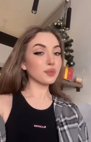 Woman with long brown hair in black tank top and plaid shirt indoors.
