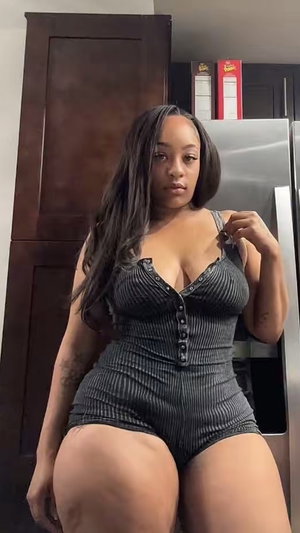 Curvy woman in gray striped romper in kitchen.