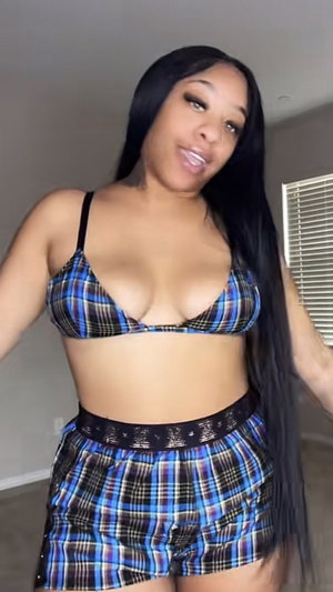 Curvy woman with long black hair in plaid bikini top and shorts indoors.