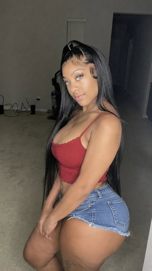 Curvy woman in red top and denim shorts posing indoors.