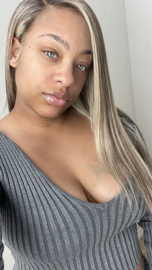 Woman with long blonde hair in grey top taking indoor selfie.
