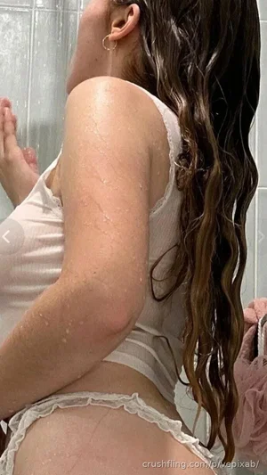 Woman with wet hair in white lingerie taking mirror selfie in bathroom.