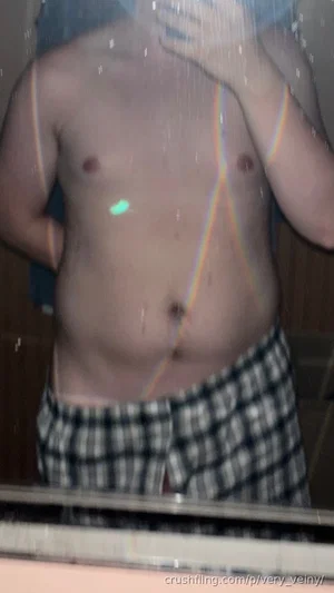 Man with bare torso and checkered shorts in shower, rainbow light effect visible.