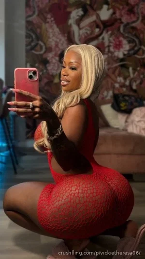 Woman with blonde hair in red lace dress posing for mirror selfie in bedroom.