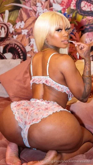 Woman with blonde bob, floral lingerie, tattooed arm, posing on bed with colorful background.
