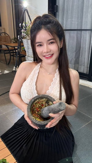 Asian woman in white lace top holding mortar indoors.