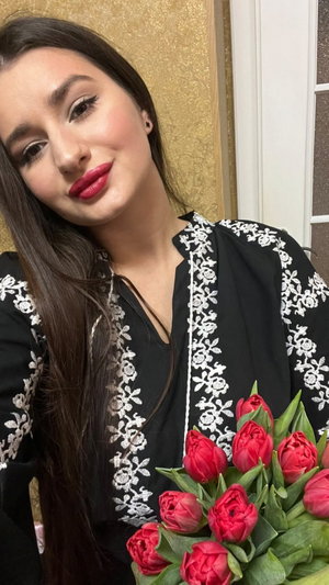 Woman with long dark hair wearing black embroidered top holding red tulips.