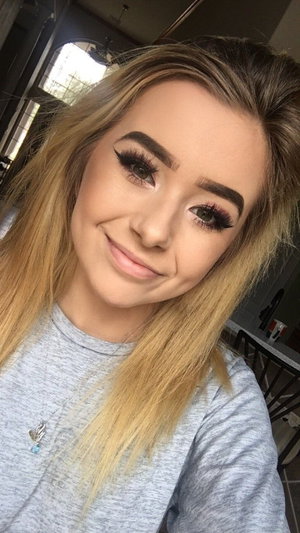 Woman with blonde hair and makeup wearing a gray shirt indoors.
