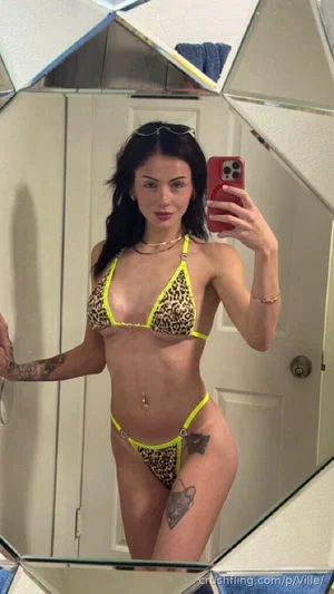 Woman in leopard print bikini with neon yellow trim takes mirror selfie in bathroom.