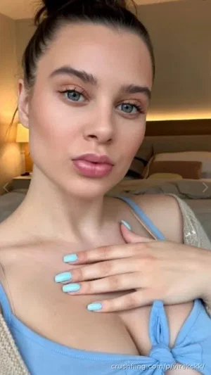 Woman with blue top and light blue nails posing in a bedroom.
