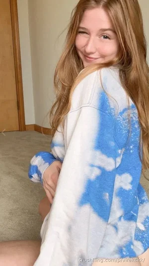 Woman with long blonde hair in a tie-dye shirt, sitting indoors, smiling at camera.