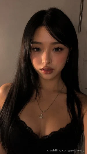 Woman with long black hair wearing black lace top, indoors, facing camera.
