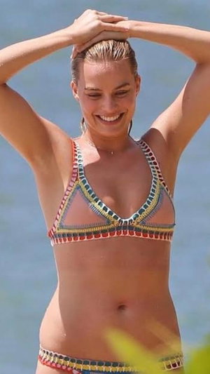 Woman in colorful bikini smiling by water, hands on head.