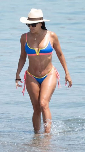 Woman in colorful bikini and hat walking in shallow ocean water.