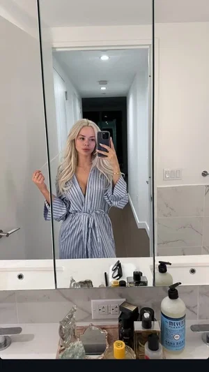 Blonde woman in striped robe taking mirror selfie in bathroom.
