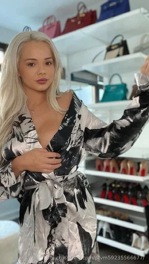 Woman with platinum blonde hair in a black and white patterned robe, standing in a closet with