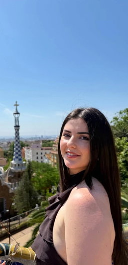 Dark-haired woman in brown top smiling outdoors with city background.