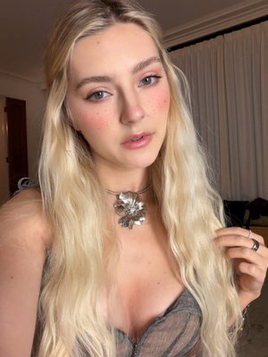 Blonde woman with long hair wearing sheer top indoors.