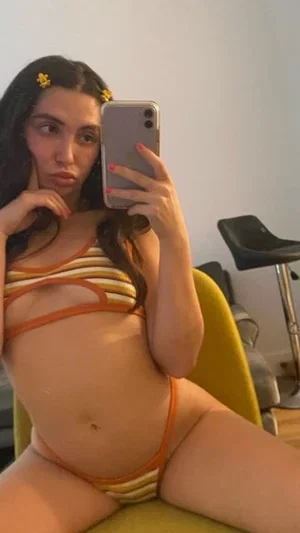Woman in orange and white striped bikini taking mirror selfie indoors.