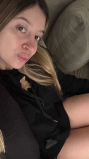 Woman with long hair in black hoodie taking indoor selfie.