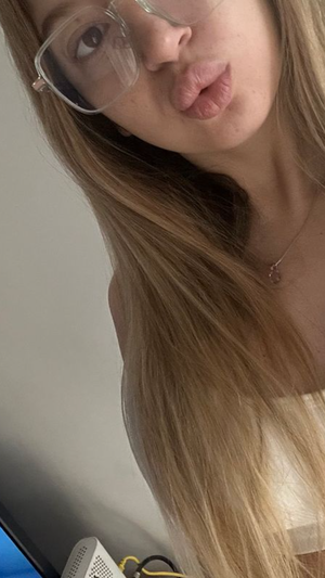 Blonde woman with glasses wearing white top indoors.