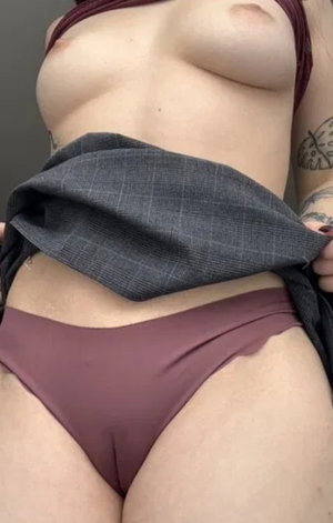 Tattooed woman lifting shirt in maroon underwear indoors.