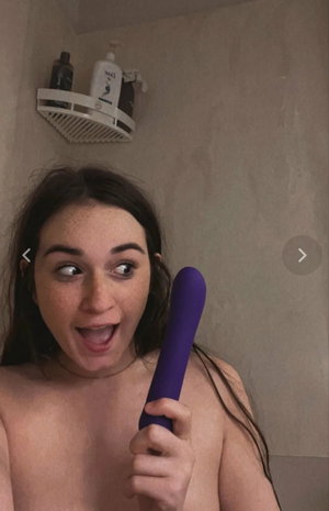Freckled woman holding purple vibrator in bathroom.