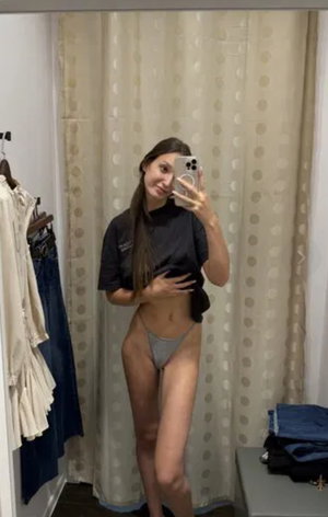 Woman in black t-shirt and grey underwear taking mirror selfie indoors.