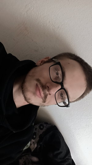 Man with glasses and beard wearing black hoodie indoors.