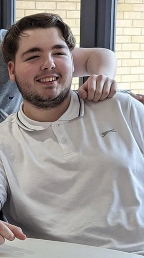 Smiling man in white polo shirt indoors with arm on shoulder.