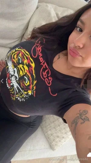 Woman with dark hair and tattoo on arm wearing black graphic tee and leggings, lying on couch.