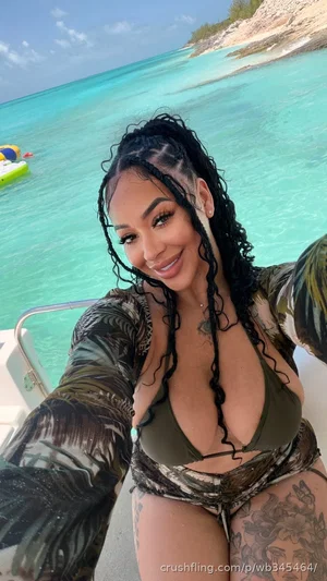 Woman in camouflage bikini on boat, turquoise water background, tattoos visible.