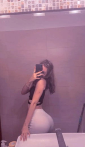 Woman in black crop top and white pants poses in bathroom mirror selfie.