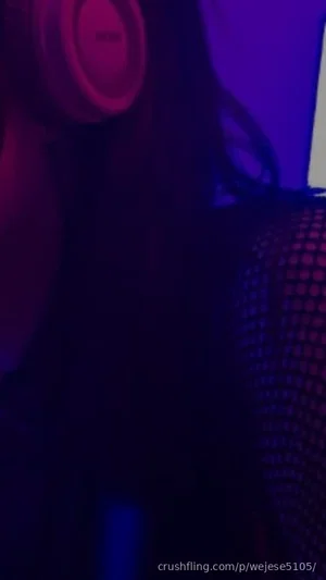 Person with long dark hair wearing headphones and mesh top in dim purple lighting.