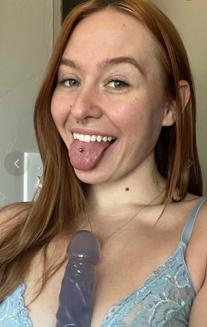 Redhead woman with piercings in blue lace top taking selfie.