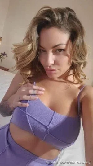 Woman with wavy hair in purple lingerie posing indoors.
