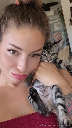 Woman with dark hair in bun holding kitten, wearing red top, indoors.