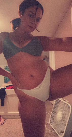 Woman in gray bra and white underwear posing indoors, one leg raised.
