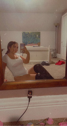 Woman in white top and black pants takes mirror selfie in bedroom.