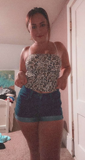 Woman in leopard print top and denim shorts standing in a bedroom.