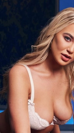 Blonde woman in white lace bra posing indoors, close-up shot.