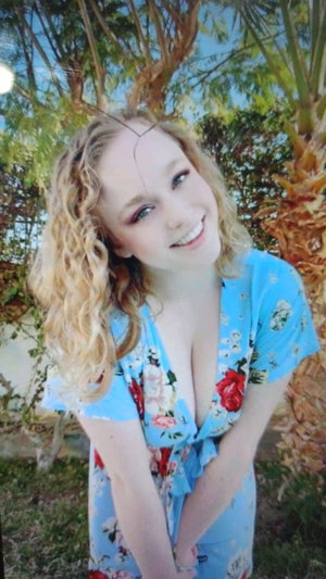 Blonde woman in blue floral dress outdoors by palm trees.