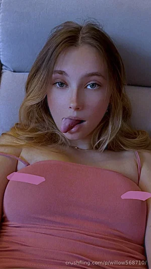 Woman with blonde hair in pink top lying on couch, tongue out.